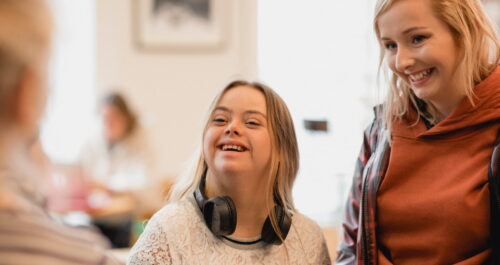 A young woman with Downs Syndrome stands with her female caregiver