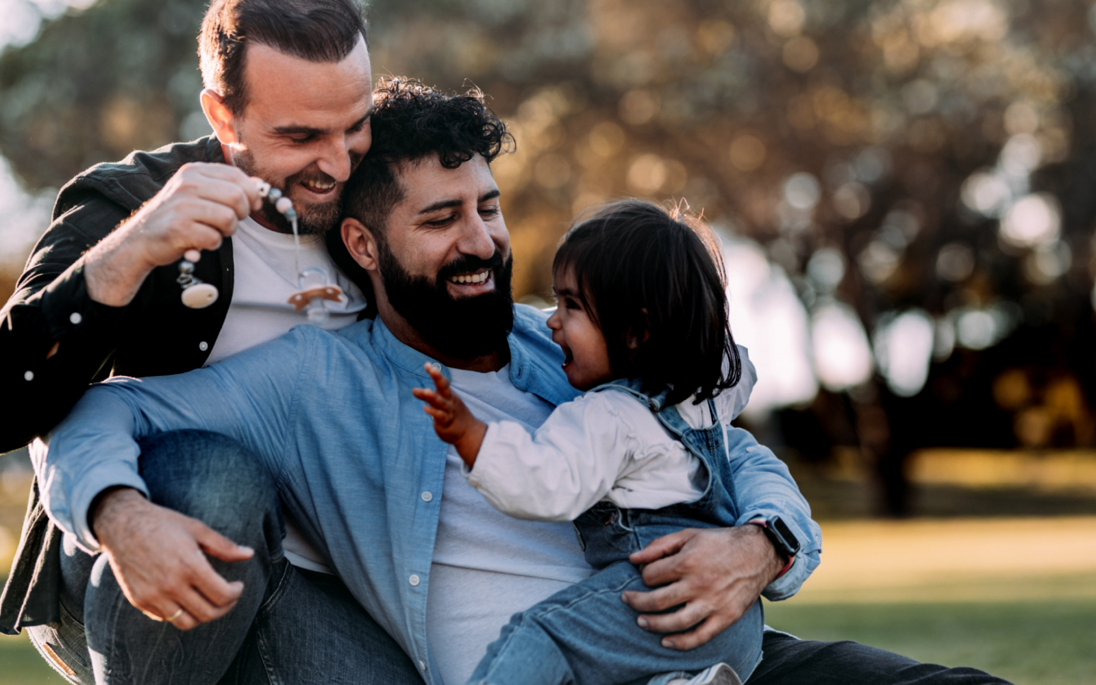 Two men and a small child embracing outside.