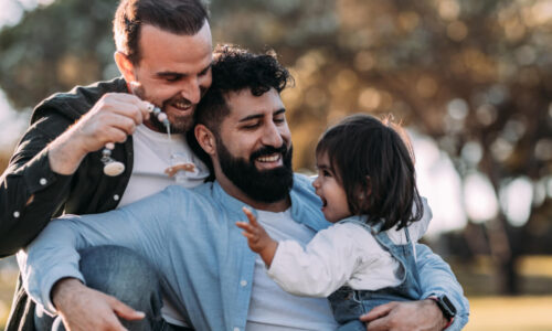 Two men and a small child embracing outside.