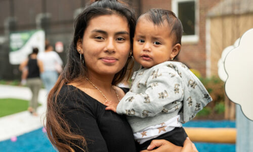 A hispanic mother and child smile at the camera at a park outdoors.