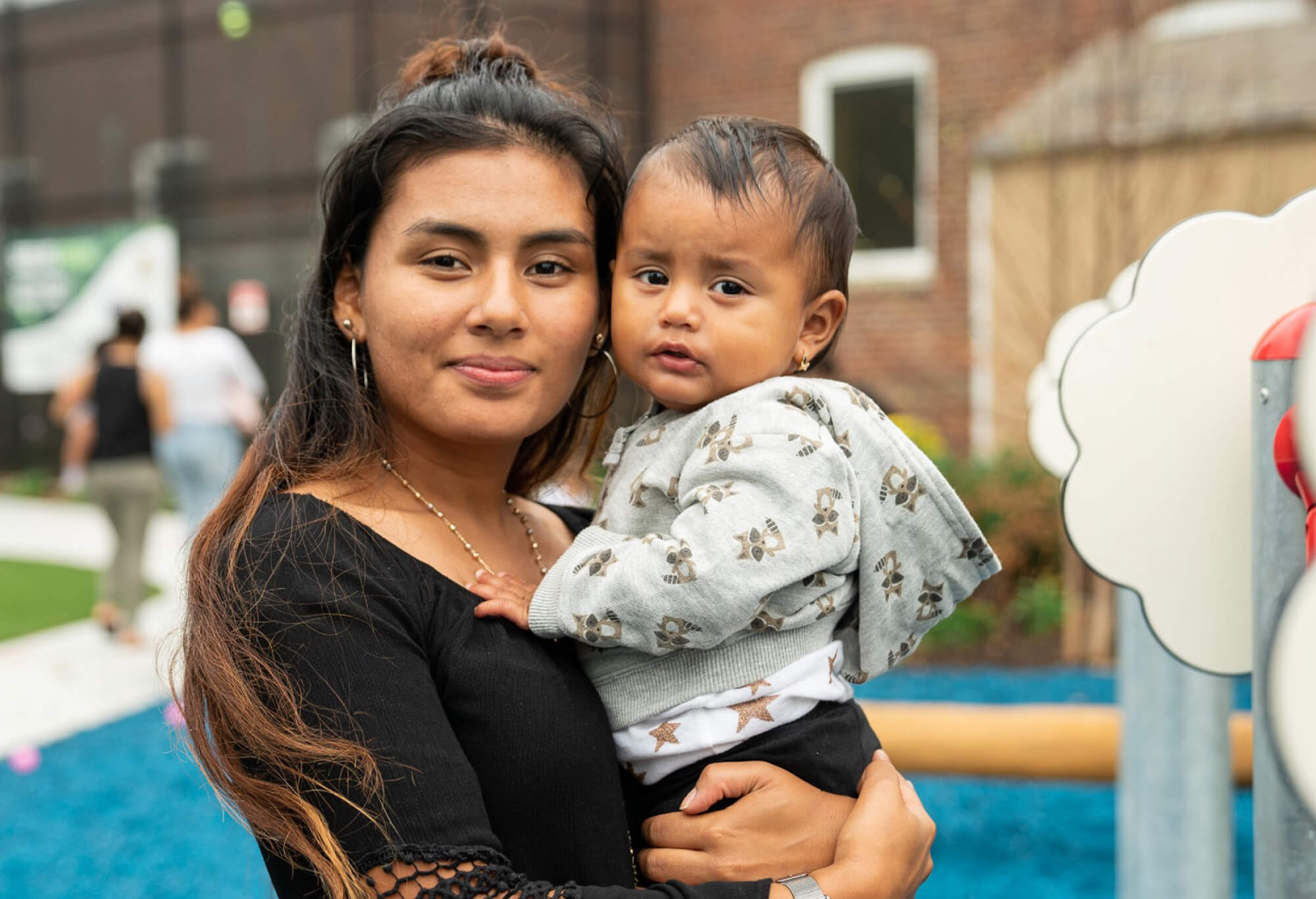 A hispanic mother and child smile at the camera at a park outdoors.